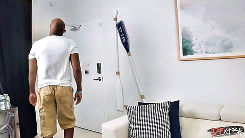 Miss Raquel adult scene: bald Black man in white tee and khaki shorts entering room