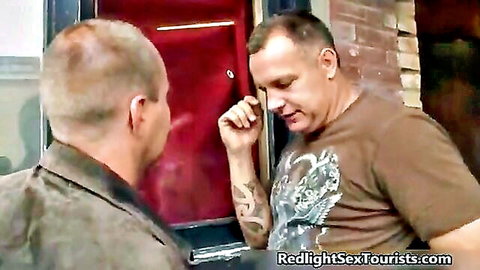 Two Caucasian men in casual clothes talk outside red door in urban setting