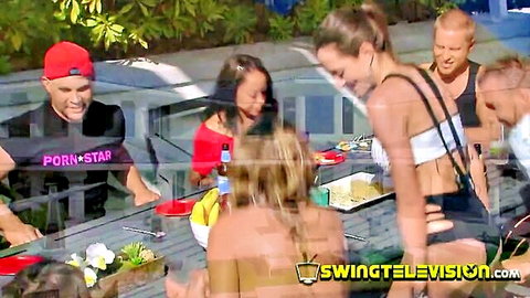 Amateur swingers at outdoor party, mixed group chatting and eating
