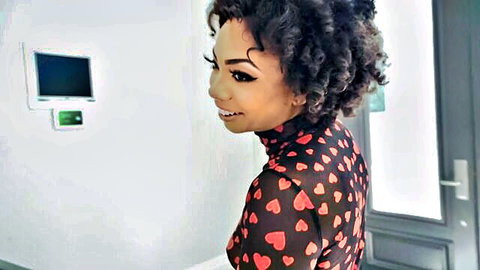 Sexy ebony woman with curly hair smiling seductively in sheer black heart-patterned top
