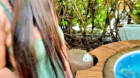 Brunette with long hair in green top teases back view by outdoor hot tub