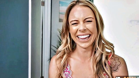 Blonde woman with long hair smiling happily showing cleavage in pink floral top with arm tattoo