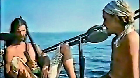 Two shirtless muscular men with long hair chatting on a boat at sea