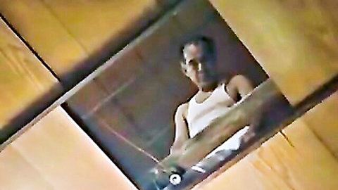Japanese man in white tank top peering through cell bars in intimate JAV scene