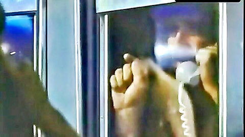 Blurry masked person using public payphone booth at night with hands gripping receiver