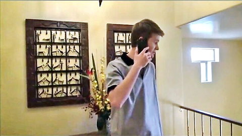 Young man in gray scrubs talking on phone in hallway with art and flowers