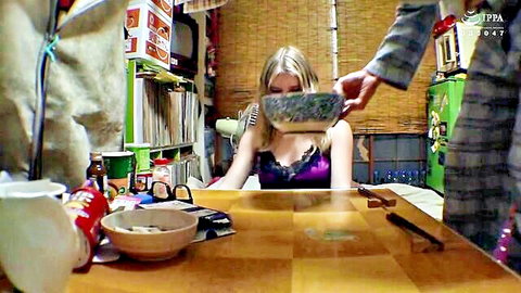 Blonde in purple lingerie sits at table as suited Asian man holds bowl of greens to her mouth showing cleavage