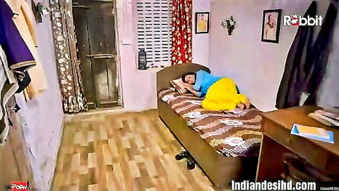 Desi woman in blue top and yellow pants lying on bed in Khat Kabbadi adult web series