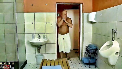 Muscular bald man in towel covering eyes teasingly in steamy bathroom