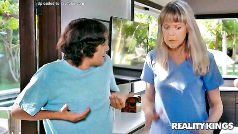 Blonde MILF nurse in tight blue scrubs talking to young curly-haired guy in kitchen