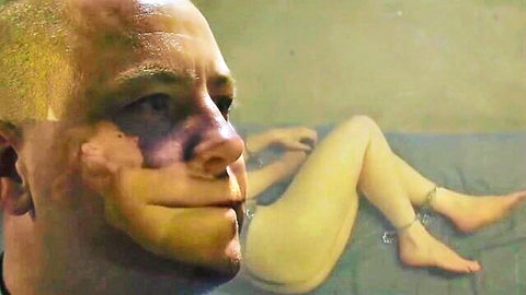 Bruised bald man gazes at chained naked female slave in BDSM transport scene