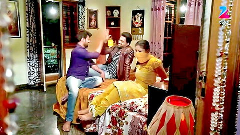 Three clothed Indian actors in yellow salwar and casual shirts chatting in living room on Zee TV show