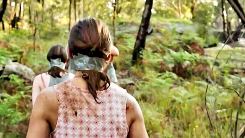 Two brunette women in dirty tank tops and headscarves walking in forest BDSM scene