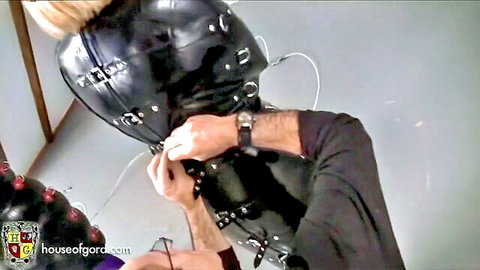 Blonde in black latex BDSM hood adjusted by dominant man