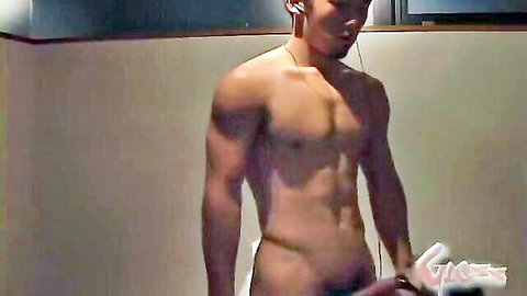Muscular Japanese hunk standing nude with earphones, teasing crotch in dimly lit room