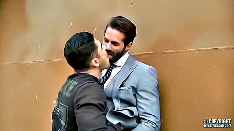 Two suited gay men passionately French kissing against a wall