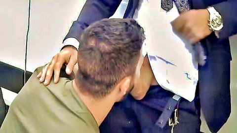 Suited man grips kneeling soldier's head pulling his open mouth to crotch bulge in domination