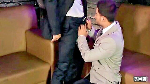 Suited man kneels groping bulging cock through pants of standing suited guy in lounge
