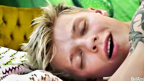 Blonde tattooed gay twink moaning ecstatically with eyes closed on bed