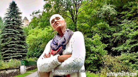 Mature Czech tour guide in Karlstejn, arms crossed outdoors in sweater and scarf