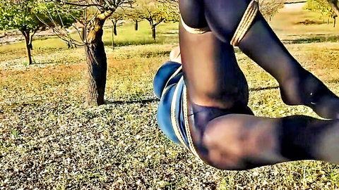 Outdoor shibari bondage in black pantyhose, bound woman in BDSM pose