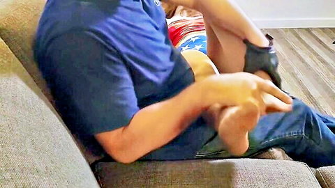 Wonder Woman defeated in patriotic flag outfit, feet held by man in BDSM tease