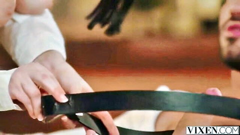 Dominant woman grips black leather belt near bearded man's open mouth in BDSM tease