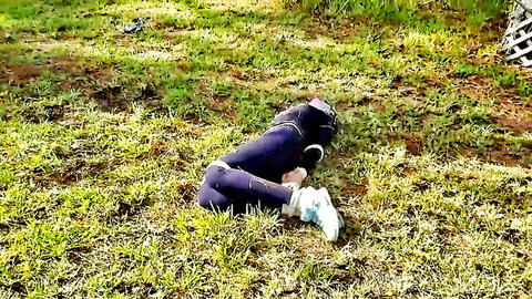 Bound jogger in purple leggings curled on grass, BDSM kidnapping tease