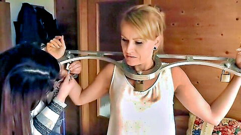 Blonde submissive locked in BDSM collar and arm spreader by Asian domme