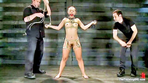 Skinny blonde MILF in gold nipple clamps and bondage harness restrained spread-eagle by two men in BDSM threesome