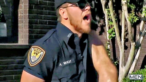 Muscular bearded cop A. McKay in tight police uniform flexing arm outdoors