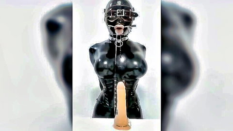 Curvy woman in black latex bondage hood and corset with dildo for deepthroat BDSM