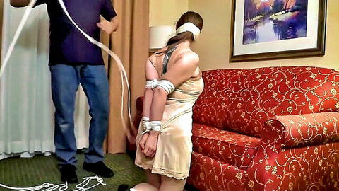 Blindfolded slim blonde in white slip bound with rope by man in BDSM bondage