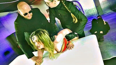 Blonde bound in red harness dominated by suited man and braided woman in BDSM threesome