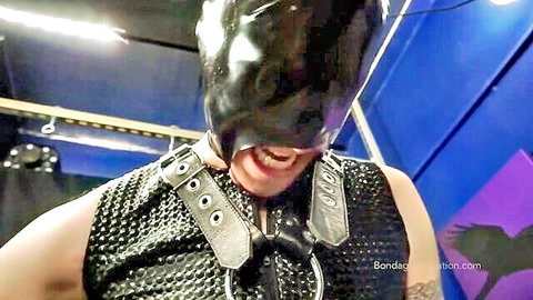 Elise Graves in black latex hood and BDSM harness, grinning through mouth opening