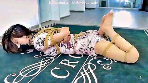 Asian woman in floral dress bound in shibari hogtie BDSM pose
