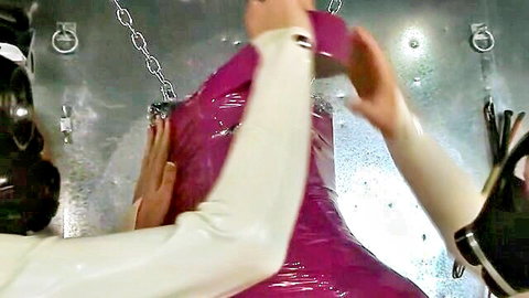 Gas-masked latex dommes in white rubber grope suspended pink latex slave in BDSM bondage