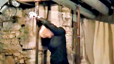 Blonde man in suit suspended upside down by chains in BDSM dungeon bondage