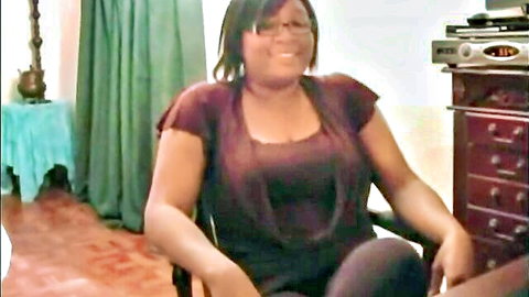 Smiling ebony MILF in tight maroon top and pants sitting teasingly in chair