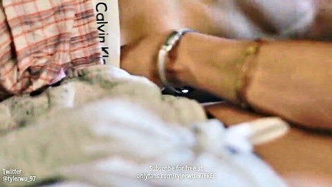 Man's toned arm in red plaid Calvin Klein shirt with silver bracelet on white bed sheets