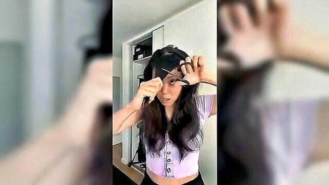 Asian woman impulsively holding scissors to long hair in pink top