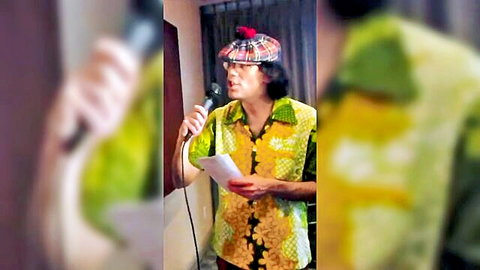 Nardwuar in yellow floral vest and tam hat holding mic and papers