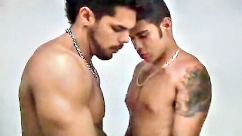 Two muscular tanned gay hunks staring intensely shirtless with tattoos and chains