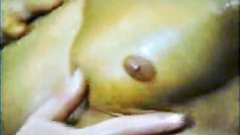 Close-up of large oiled breast being groped by hand, exposed nipple