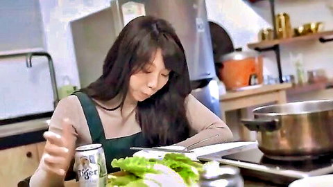 Asian woman in green apron holding beer can with lettuce, kitchen tease