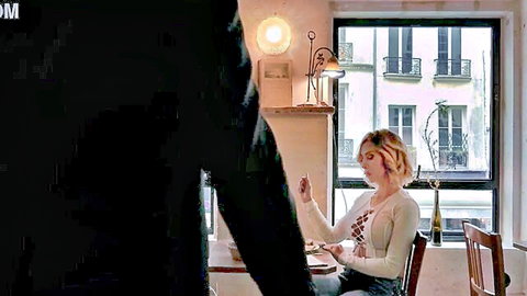 Blonde woman in lacy top sitting at table with man standing behind her in cozy Parisian room