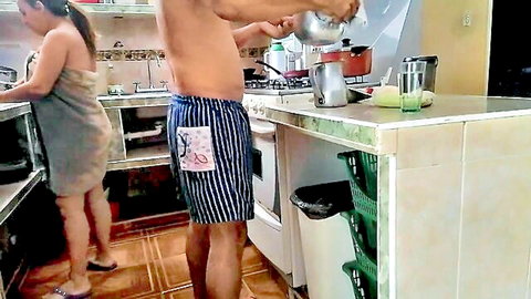 Amateur wife in towel bends over kitchen sink while shirtless hubby in striped trunks pours drink
