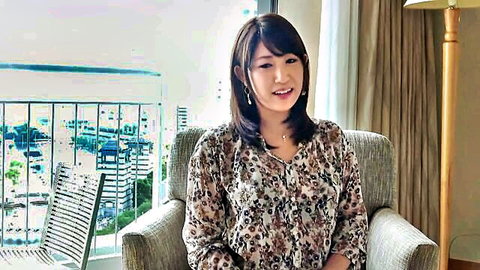 Smiling Asian woman in patterned blouse sitting in hotel room chair with city view