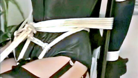 Latex-clad BDSM slut bound with white straps exposing gartered stockings thighs