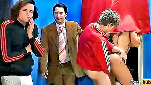 Curly-haired guy in red tracksuit fucks blonde babe doggystyle in booth while suited man watches